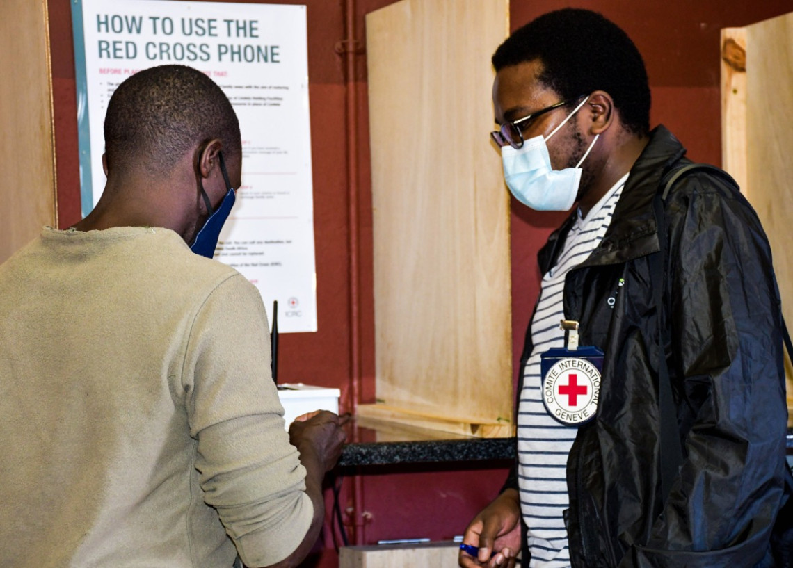 ICRC official, Talent Moyo, helps a man use the GSM phone which is currently being provided at the Lindela Repatriation Centre in South Africa. 